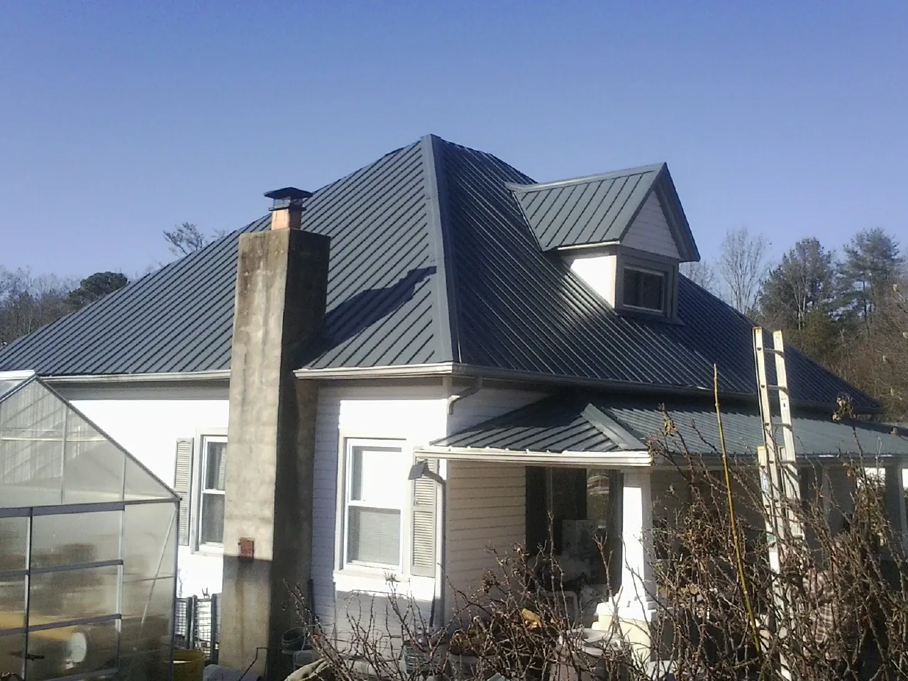 Dark blue standing seam metal roof on a white farmhouse with dormer — Slate & Tile Roof Repair by Roofing Brothers in Constantine