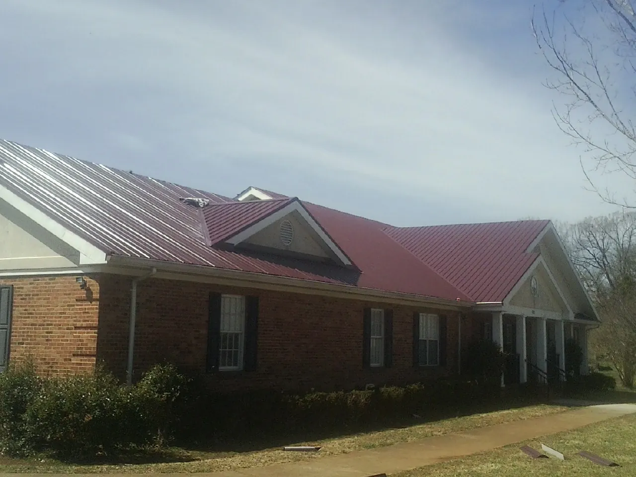 Red metal roof with gabled entries on a long brick building, from a Hail Damage Roof Repair job in Constantine