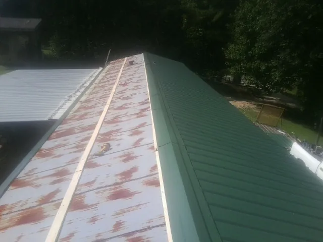 Old rusted panels beside newly installed green metal roofing — Wind Damage Roof Repair by Roofing Brothers in Constantine