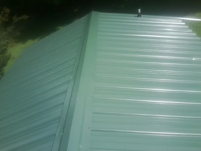 New green metal panels meeting at the ridge of a roof — Flat Roof Repair work by our crew in Constantine