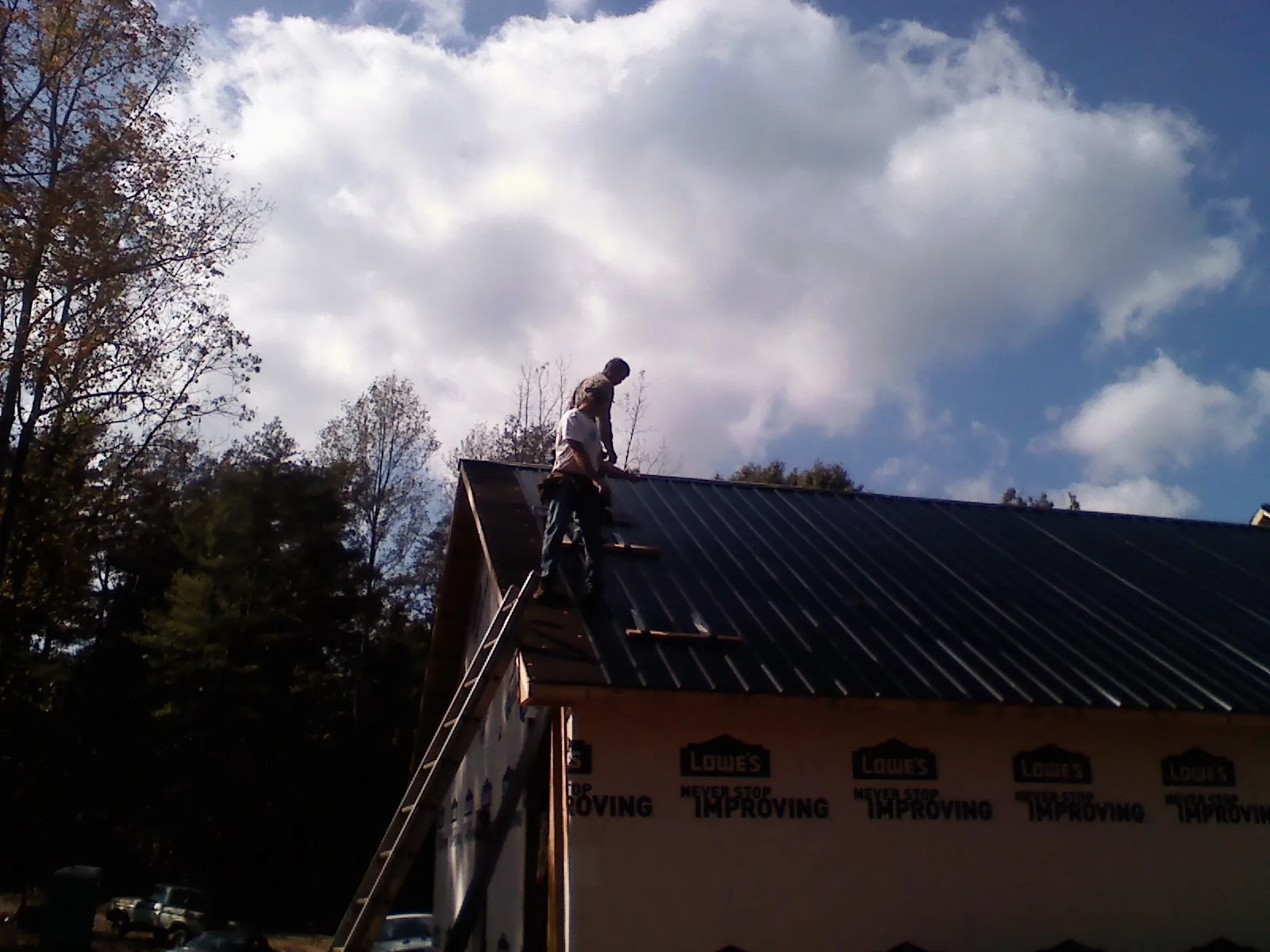 Roofer fastening dark metal panels high against a cloudy sky, from a Roof Inspection job in Constantine
