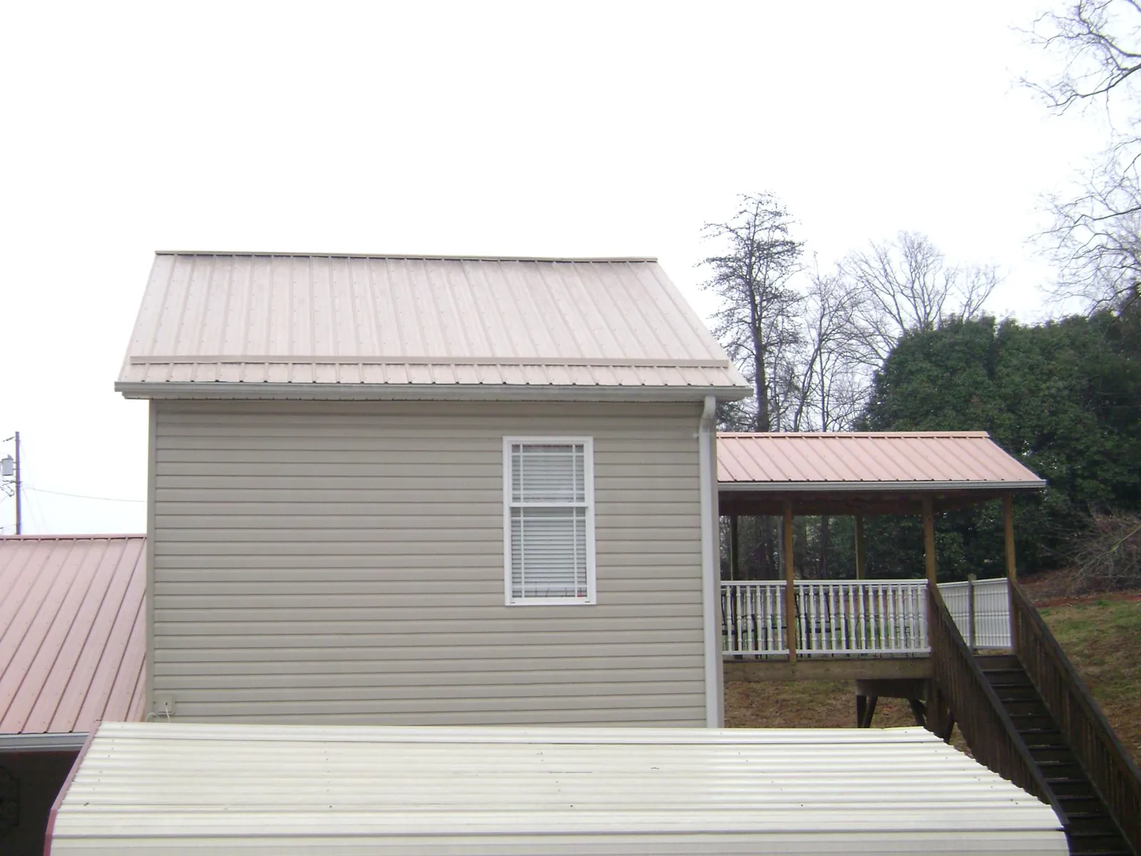 Tan metal roofs on a two story addition and attached porch, from a Roof Replacement job in Constantine